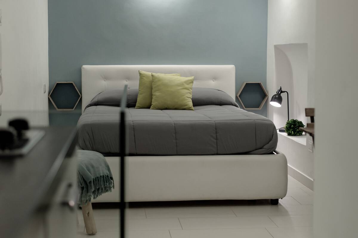 A modern bedroom with a large bed, a bedside table, a lamp, and a wall-mounted light fixture.