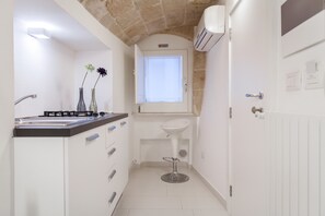 A compact kitchen with a gas stove, white cabinets, and a small window above the sink. - B&B Le Caravelle (Monopoli)