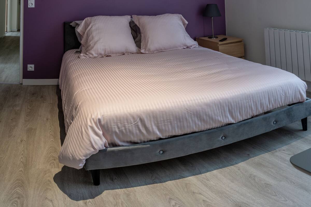 Een slaapkamer met een bed, nachtkastje, lamp, stoel en een tafel.