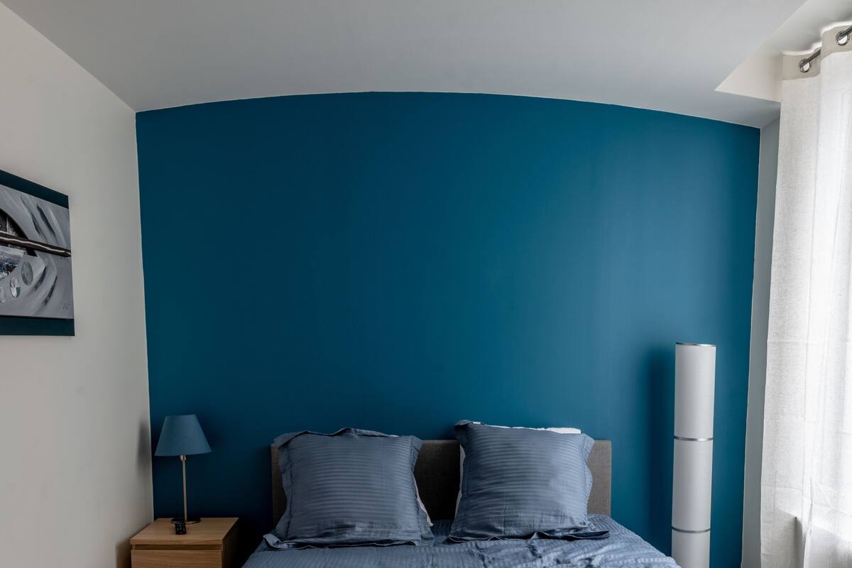 Een slaapkamer met een bed, nachtkastje, lamp en stoel.