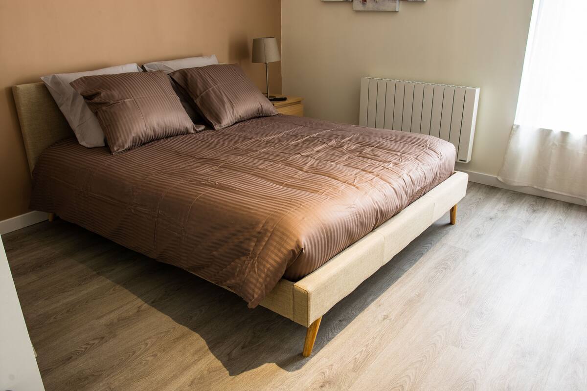 Een slaapkamer met een houten bed, nachtkastje, lamp en een radiator.