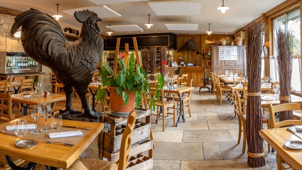 A restaurant interior with wooden furniture, a large rooster decoration, and a variety of plants. Tables are set with wine glasses and cutlery. - La ferme saint Jacques (Chatellerault)