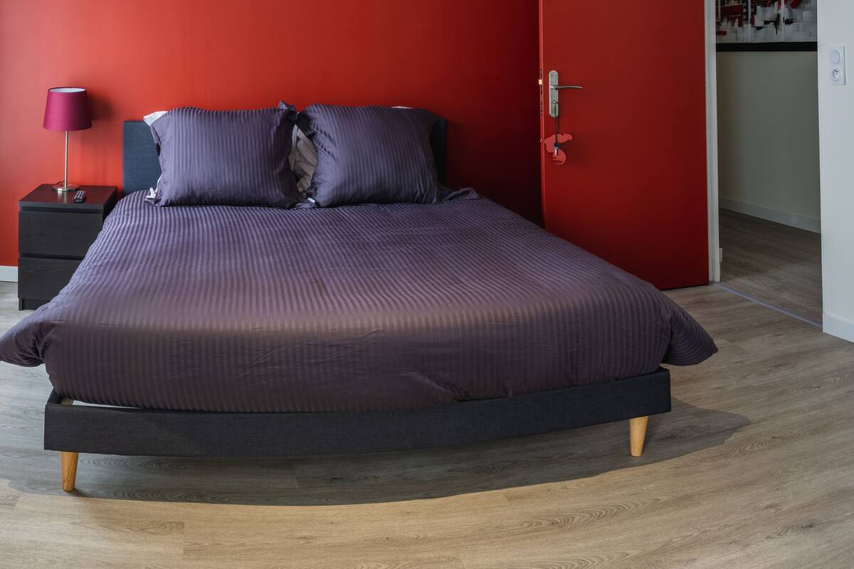 Een moderne slaapkamer met een bed, een nachtkastje, een lamp en een rode wand.