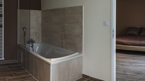 A bathroom with a bathtub and a shower, a bedroom with a bed and a wooden floor. - La ferme saint Jacques (Chatellerault)