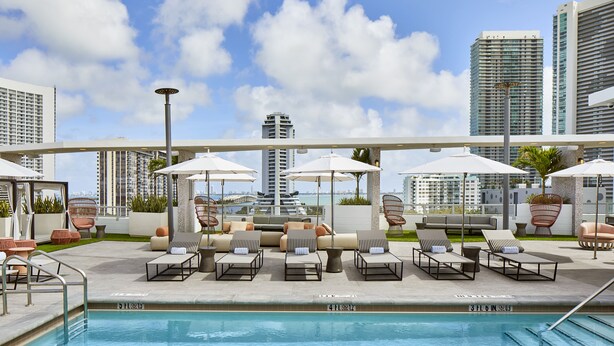 A rooftop pool area with lounge chairs and umbrellas, surrounded by high-rise buildings.