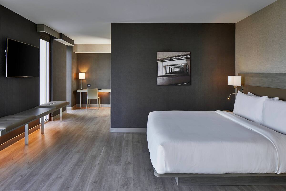 A modern hotel room with a large bed, a flat-screen TV, a desk, and a chair.