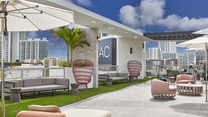 An outdoor seating area with modern furniture, a city view, and a building with 'AC' signage.