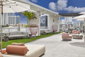 A modern hotel room with a large bed, a sofa, a small table, a TV mounted on the wall, and a large window offering a view of the city. at AC Hotel Miami Wynwood