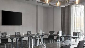A conference room with a long table, chairs, a large screen, and a modern ceiling design.
