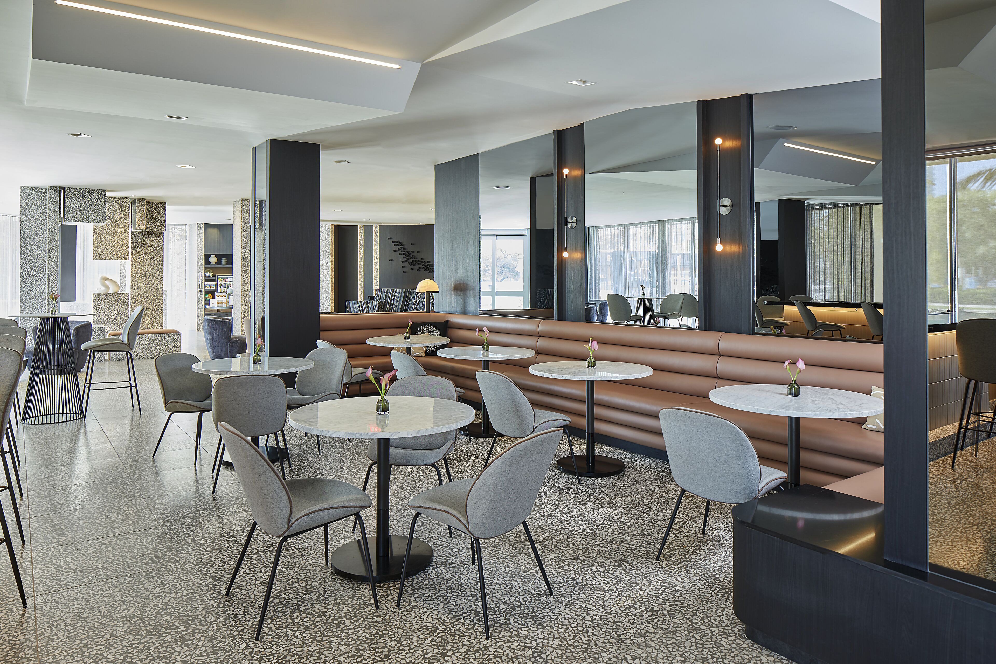 A modern restaurant with round tables, grey chairs, and a central seating area with benches.