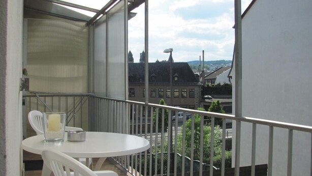 En balkon med et hvidt bord og stole, et glas vand og et stearinlys.
