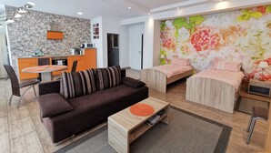 En moderne stue med sofa, to senge, spisebord og et køkkenområde med en stenvæg.