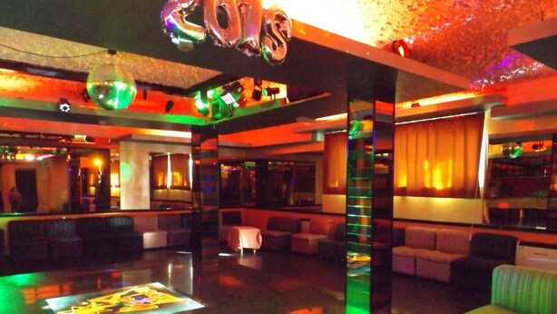 Zona de bar moderna con separador de vidrio, asientos y decoraciones iluminadas.