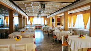 Un comedor amplio con varias mesas, cada una con mantel blanco y sillas anaranjadas.