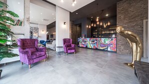 A modern lobby with a bar area, two purple armchairs, a gold sculpture, and a colorful mural. - Amarant Apart Hotel (Kyiv)
