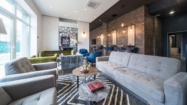 A modern living room with a grey sofa, a coffee table, and a patterned rug. There are two armchairs and a green sofa in the background. - Amarant Apart Hotel (Kyiv)