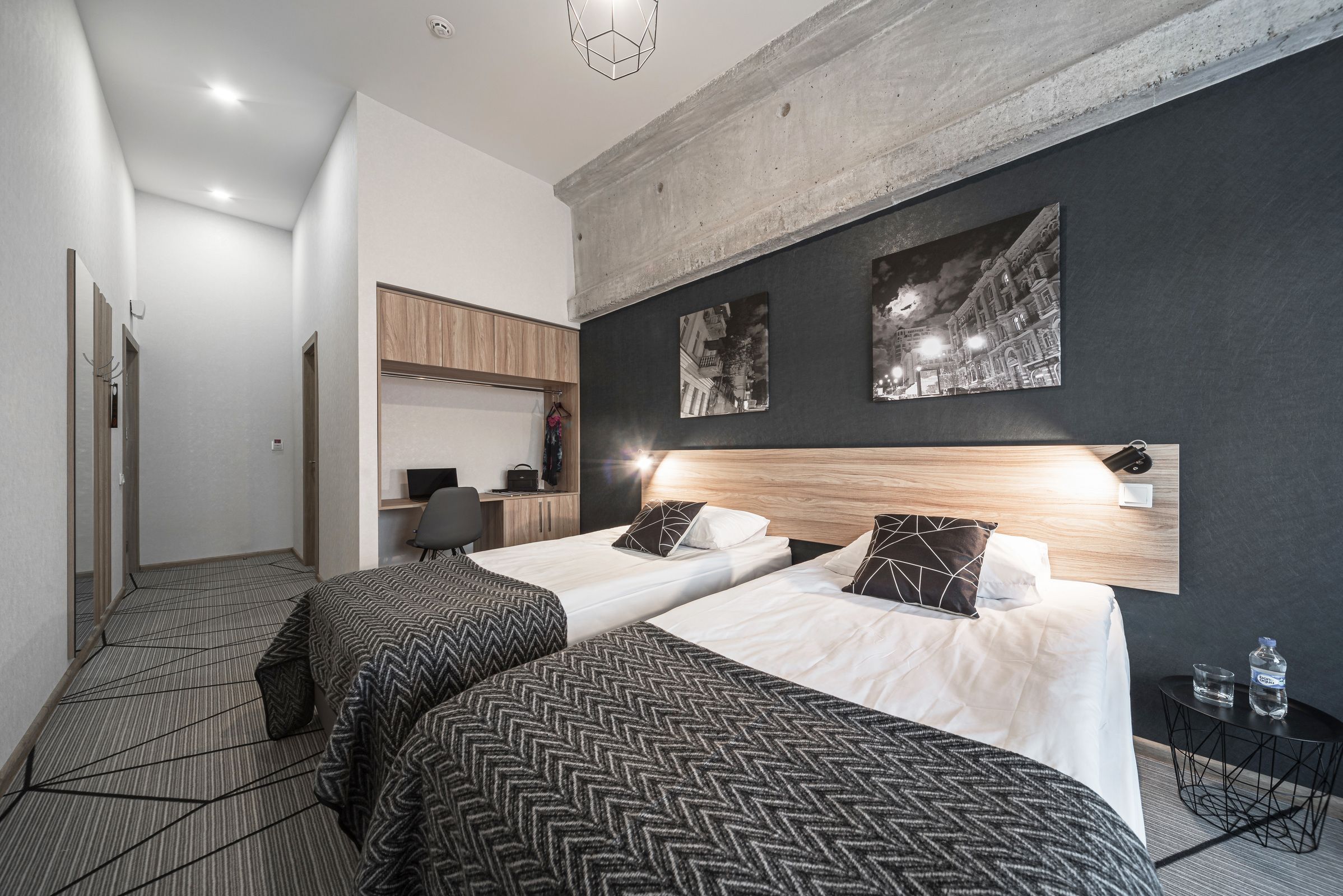 Habitació d'hotel moderna amb dos llits, un panell de fusta al capçal, una taula de treball i una televisió penjada a la paret.