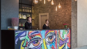 A reception area with a colorful abstract painting, a brick wall, hanging light bulbs, and a shelf with bottles. - Amarant Urban Hotel (Kyiv)