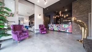 A modern lobby with two purple armchairs, a bar area with a colorful mural, and a golden sculpture. - Amarant Urban Hotel (Kyiv)