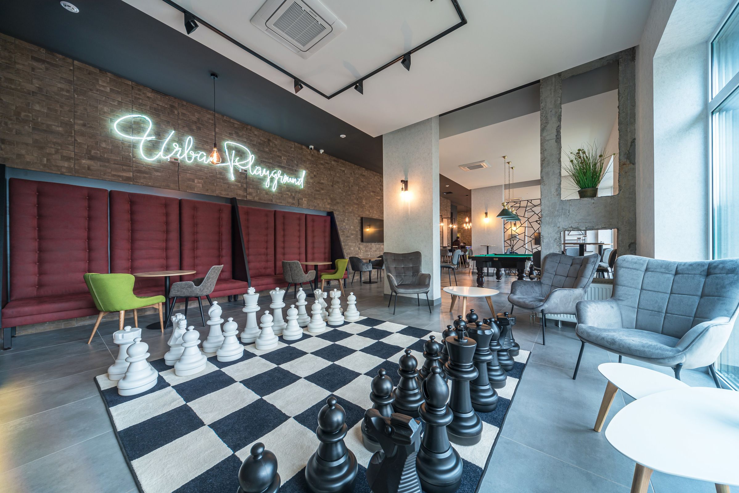 A modern lounge area with a large checkered carpet, chess pieces, and seating arrangements.
