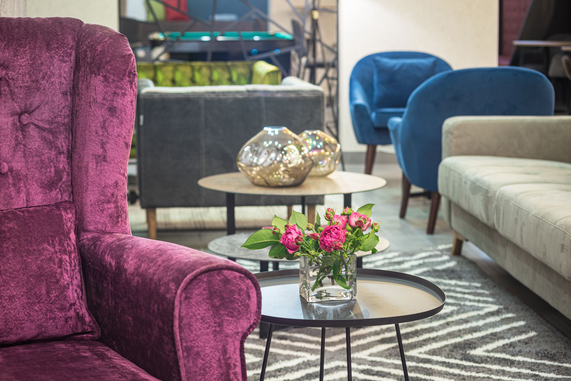 A living room with a purple armchair, a round coffee table with a vase of flowers, and a grey sofa.