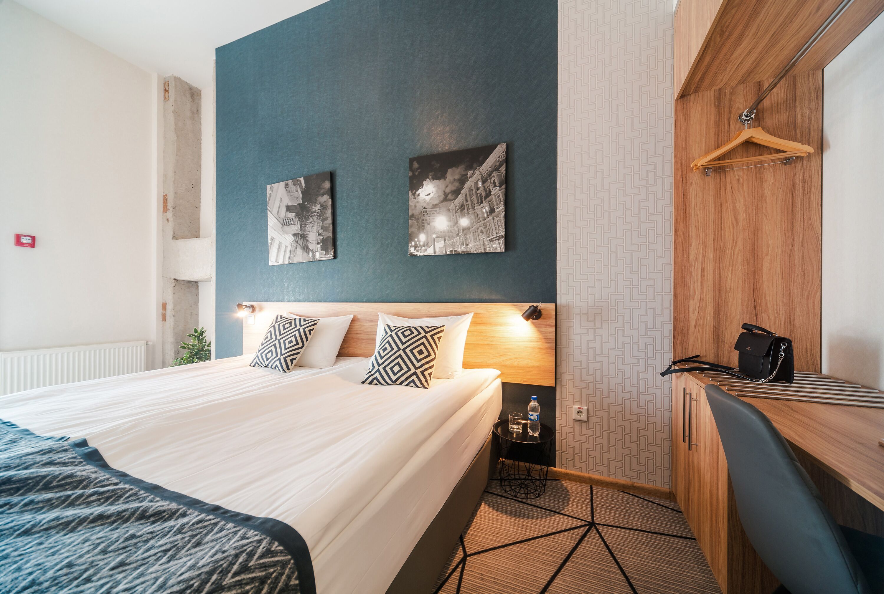 Une chambre d’hôtel avec un grand lit, un bureau avec une chaise, une armoire et deux tableaux accrochés au mur.