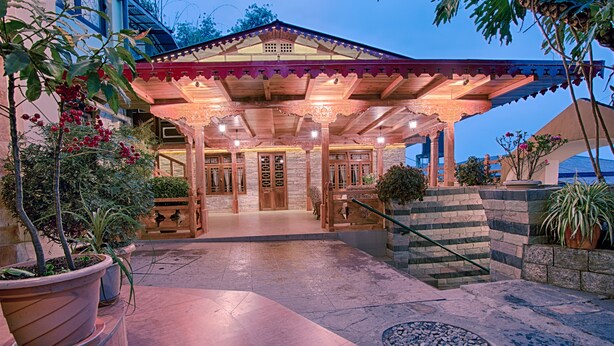 A covered outdoor area with a stone floor, potted plants, and a wooden entrance. - Netuk House (Gangtok)