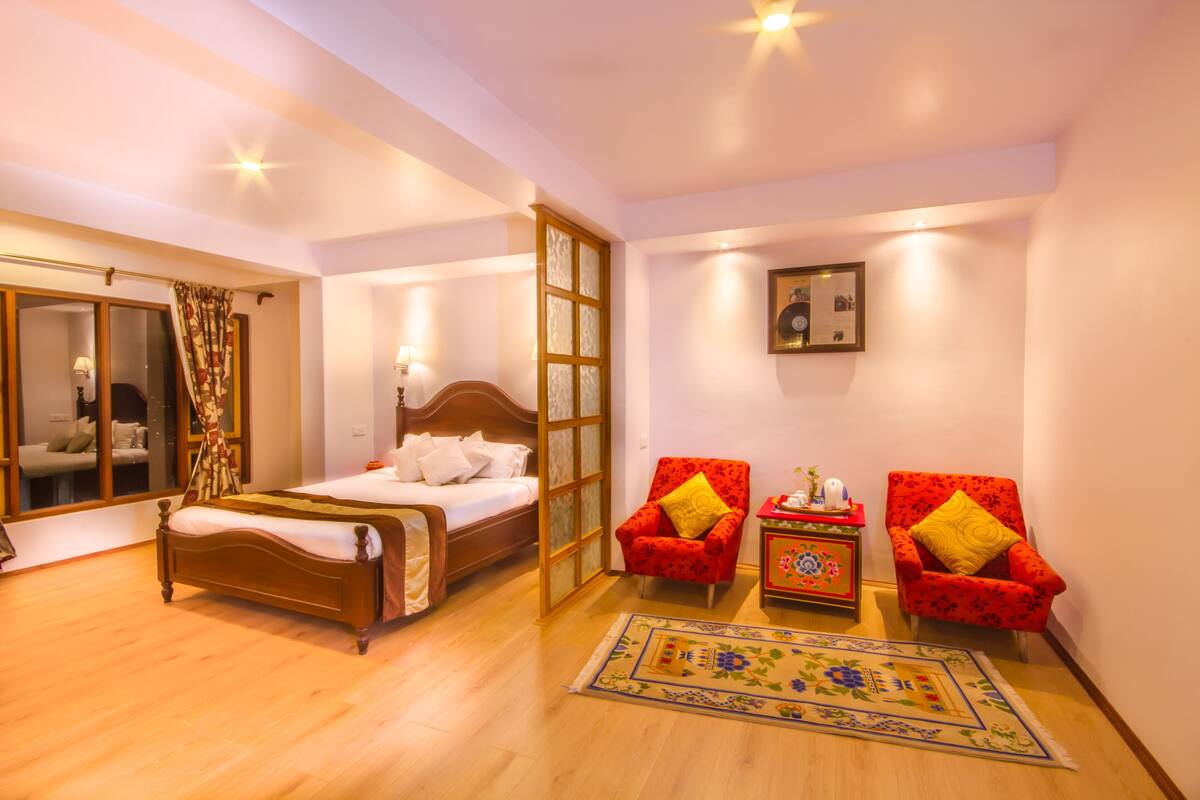 A bedroom with a wooden bed, a red armchair, a small table with a decorative item, and a mirror.