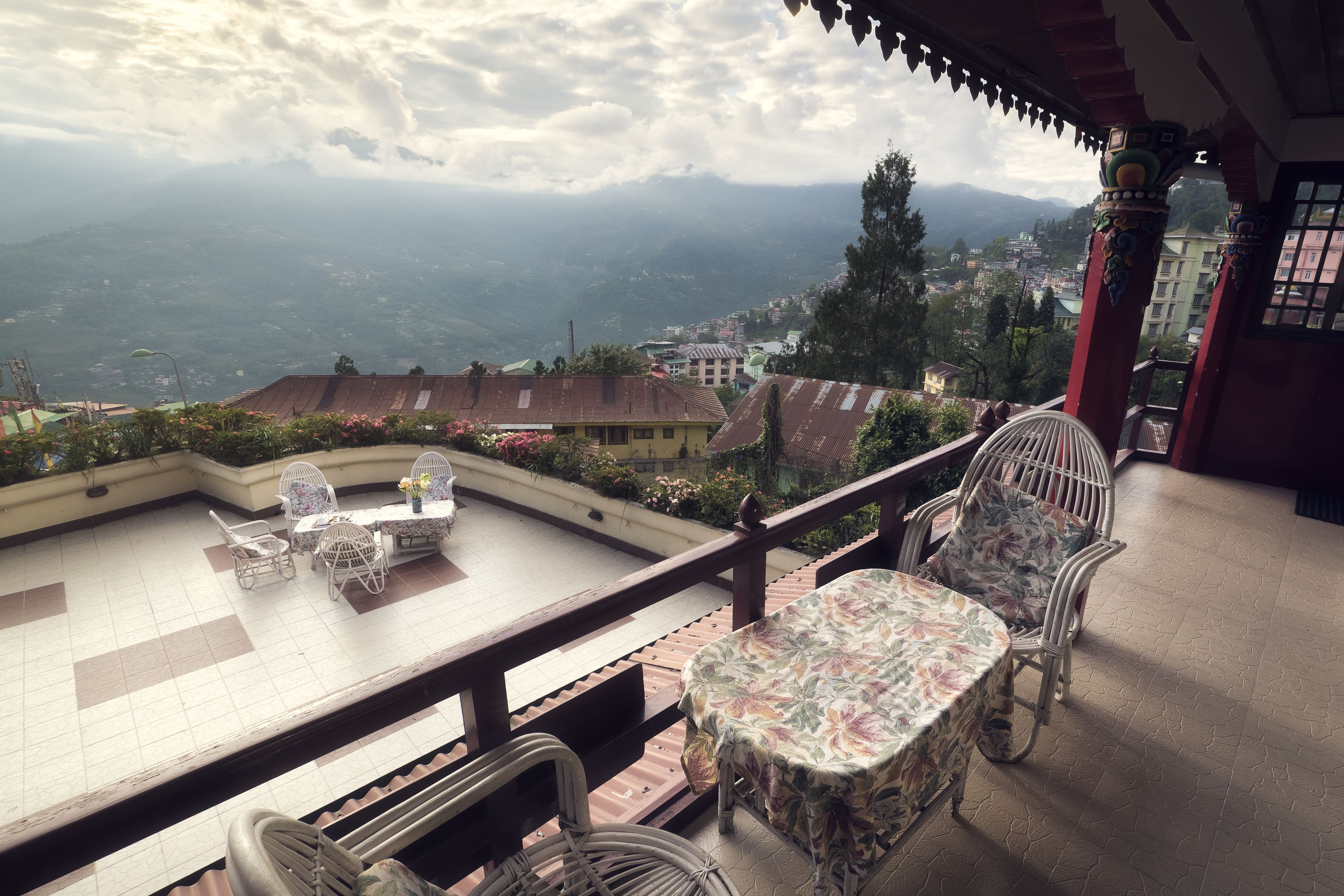 A terrace with wicker furniture and a table, overlooking a mountainous landscape.