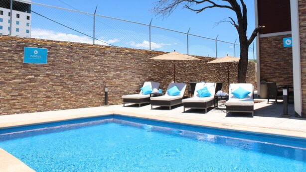 A swimming pool with lounge chairs and umbrellas, a brick wall, and a sign for 'noktos'.