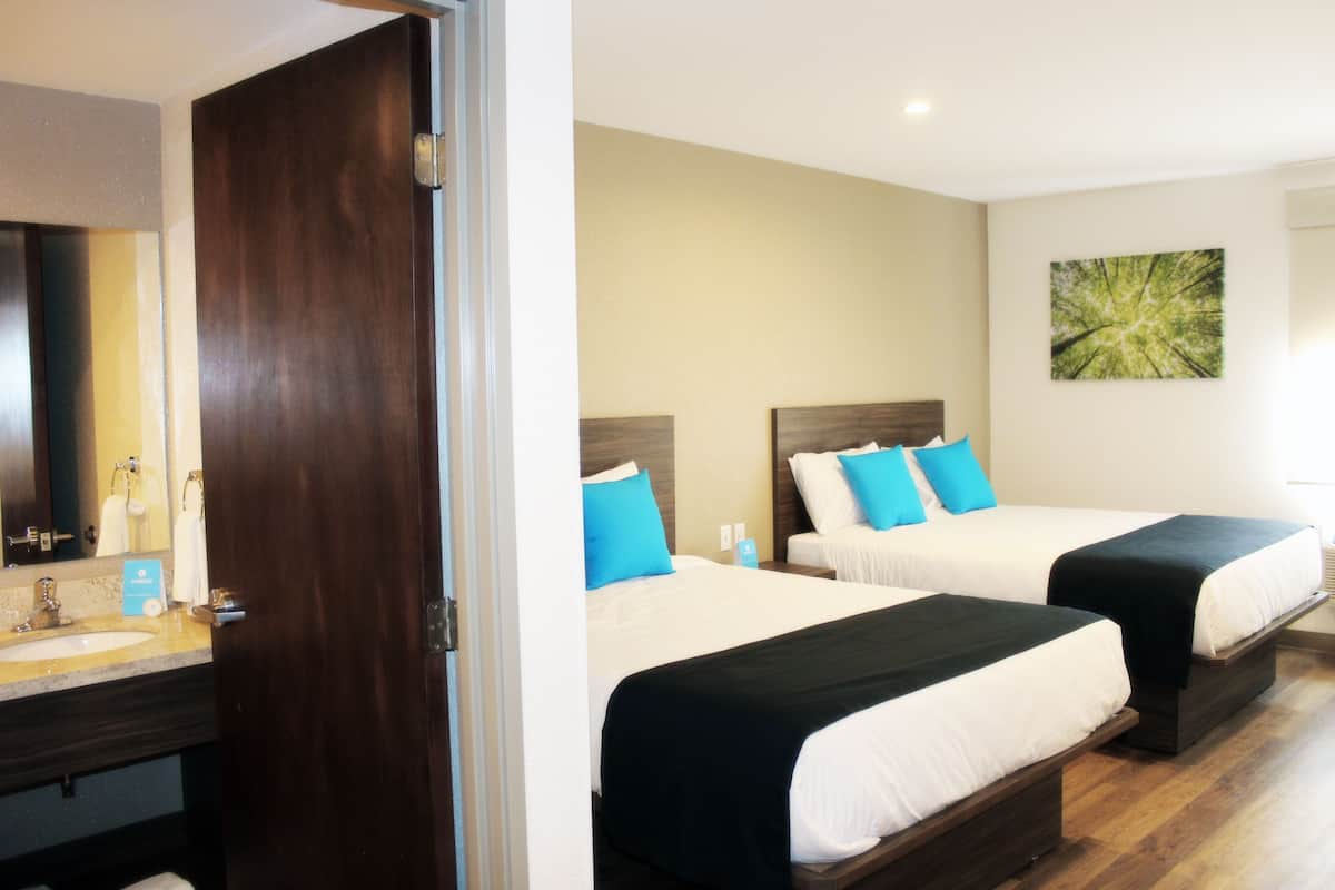 A hotel room with two beds, a bathroom with a sink, and a painting on the wall.