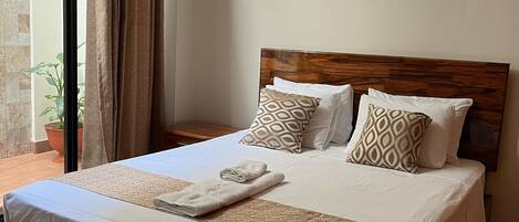 Una cama bien hecha con cabecera de madera, ropa de cama blanca y almohadas estampadas.