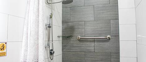 A shower with a glass door, a handrail, and a showerhead.