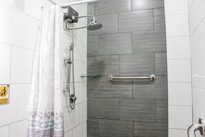 A shower with a glass door, a handrail, and a showerhead.