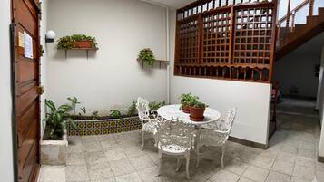 A small patio with a round table and white chairs, surrounded by potted plants and a decorative wooden screen.