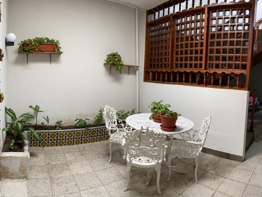 A small patio with a round table and white chairs, surrounded by potted plants and a decorative wooden screen.