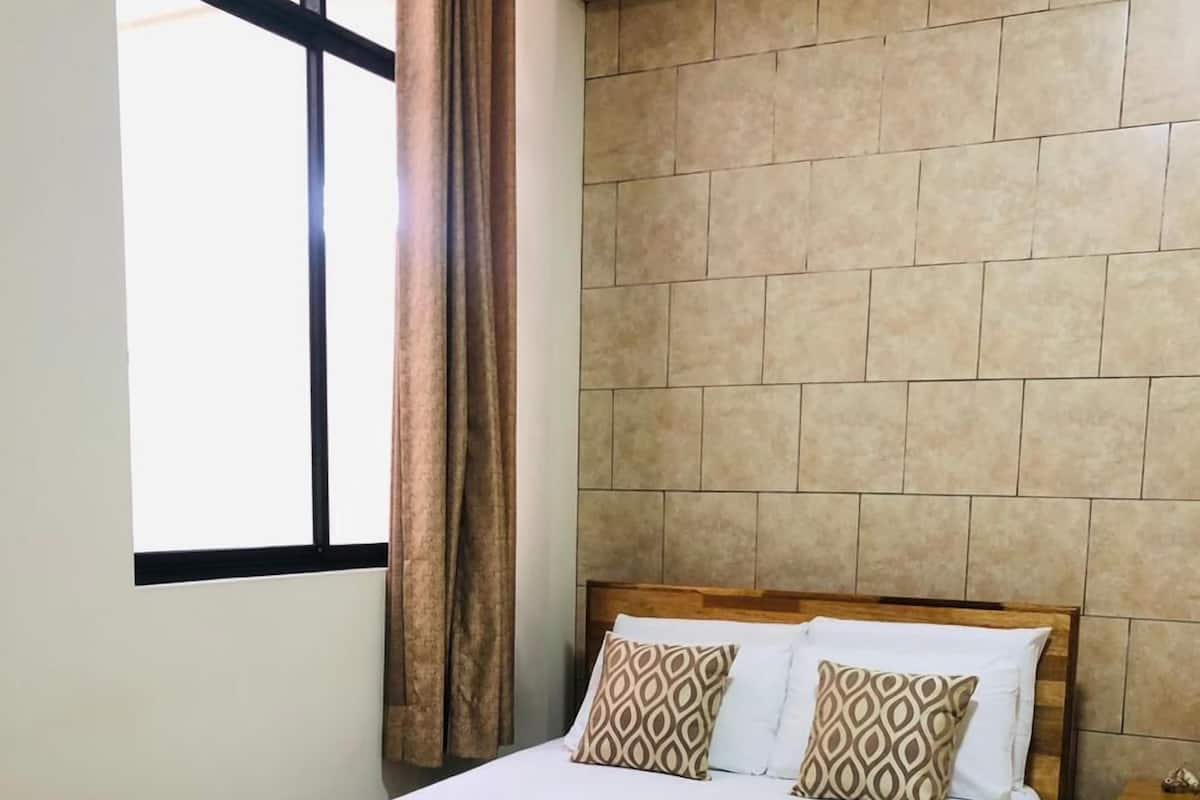 A neatly made bed with a patterned pillow, a wooden headboard, and a window with curtains.