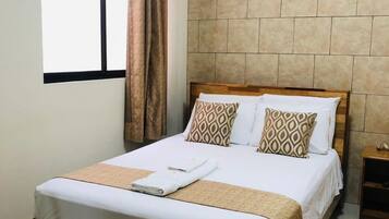 Una cama bien hecha con un cojín estampado, un cabecero de madera y una ventana con cortinas.