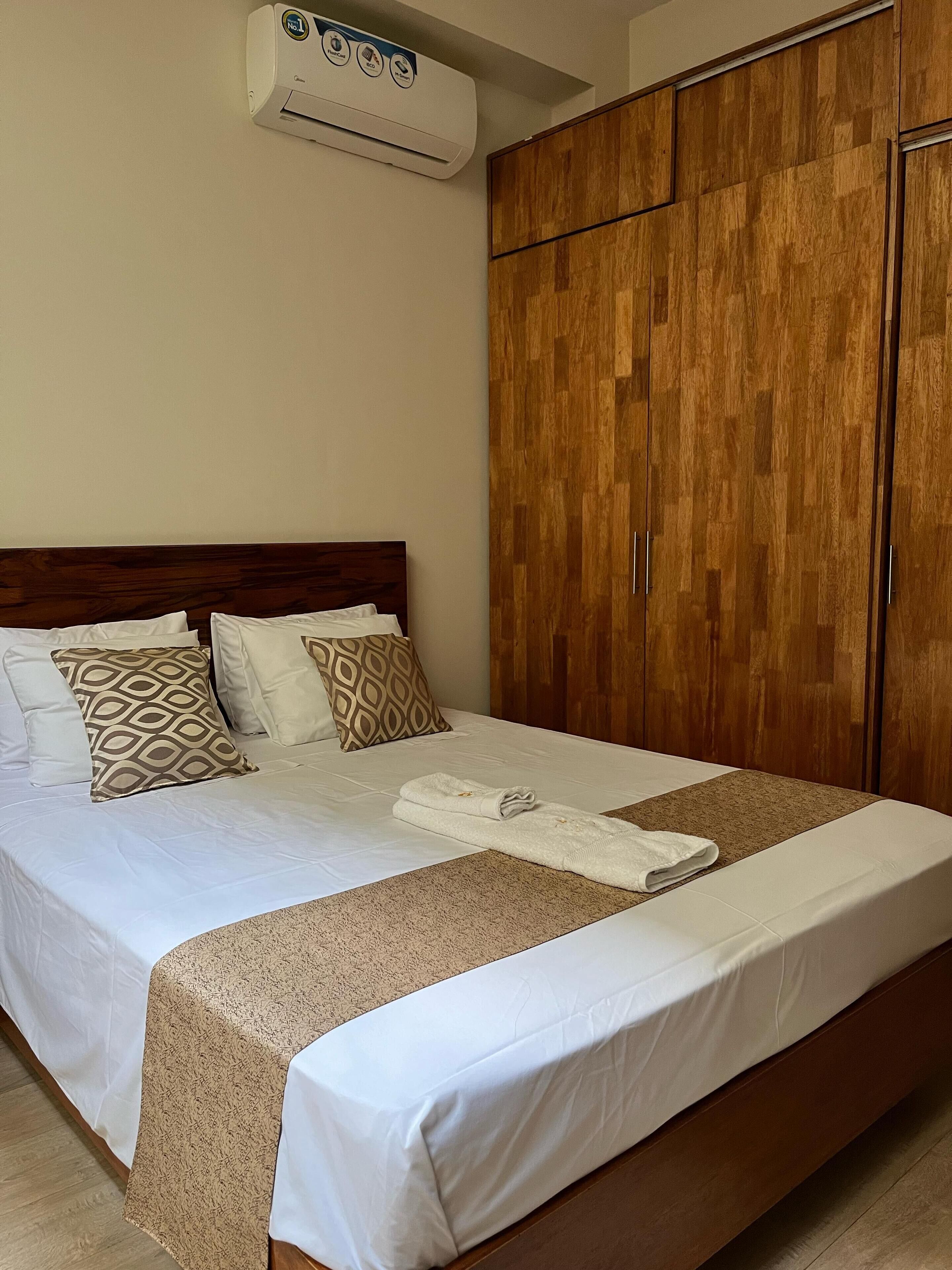 Habitación de hotel con una cama grande, armario de madera y aire acondicionado.