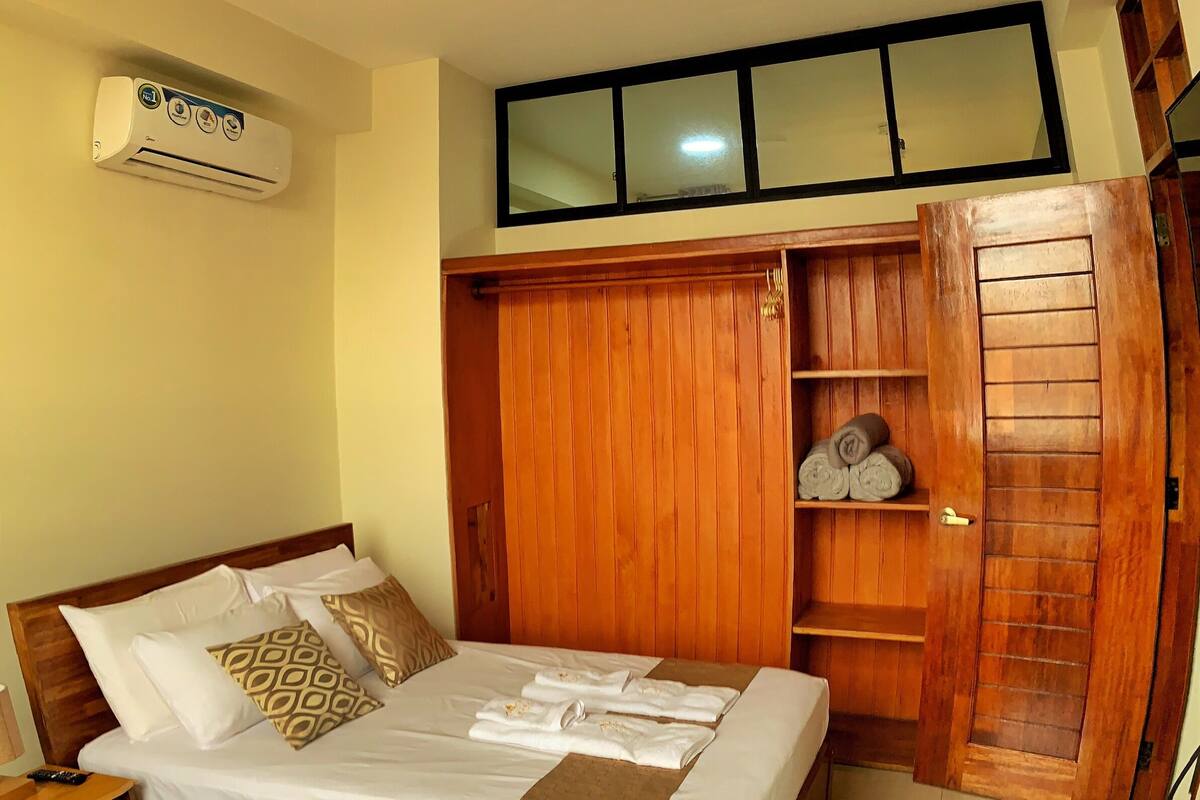 A hotel room with two beds, wooden wardrobe, and a ceiling fan.
