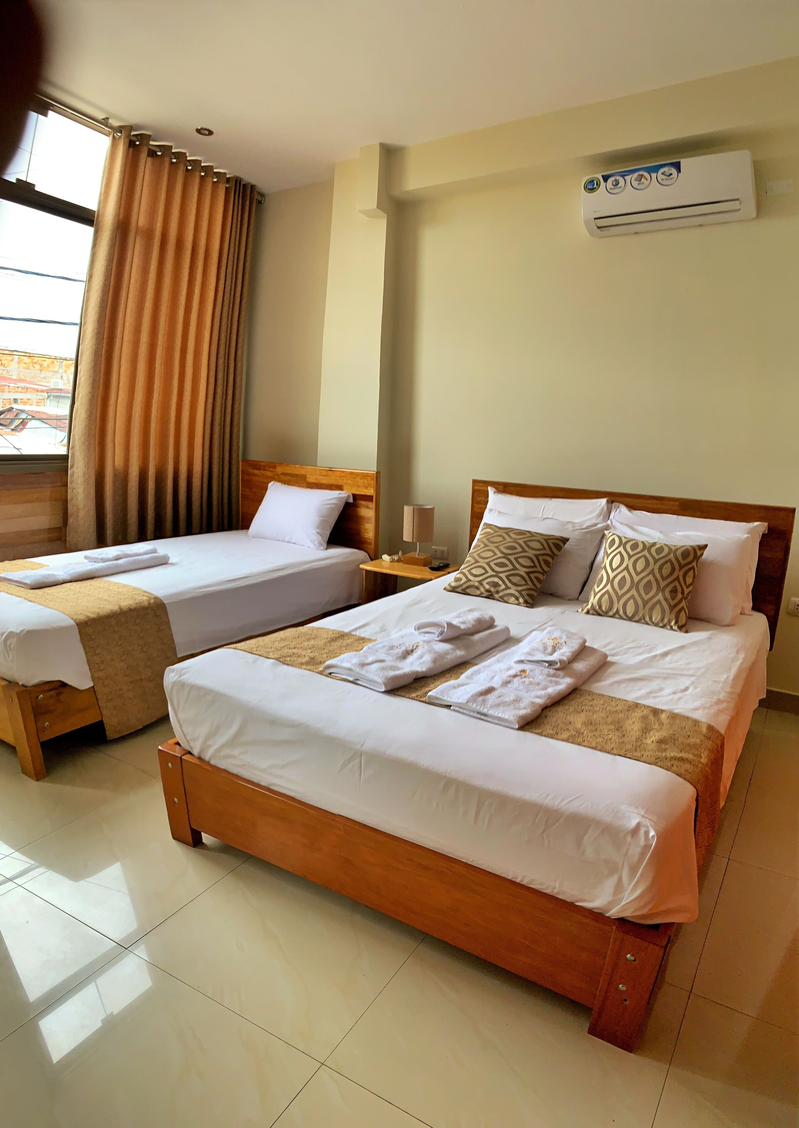 Una habitación de hotel con dos camas individuales, una cama doble más grande y un equipo de aire acondicionado en la pared.