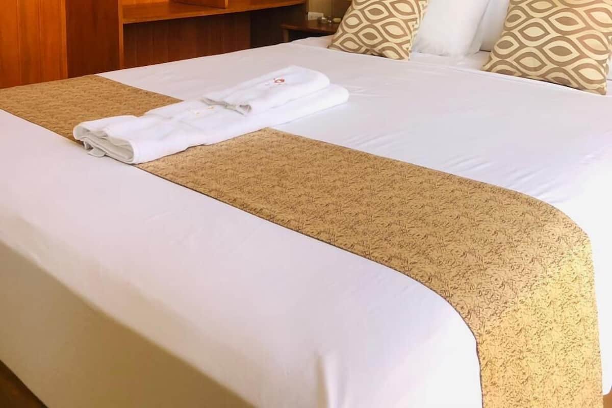 A hotel room with a neatly made bed, a wooden wardrobe, and a wall-mounted air conditioner.