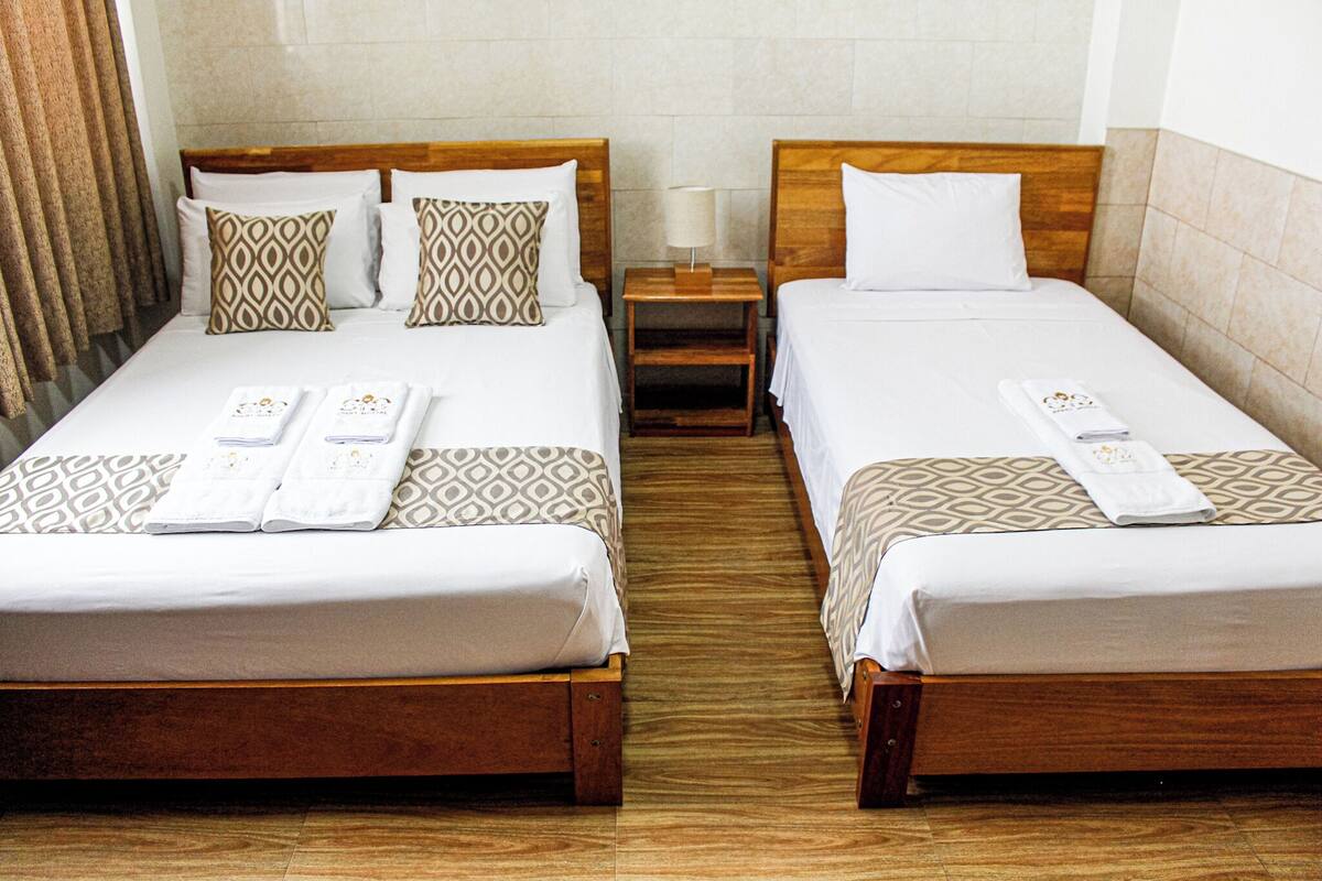Two single beds with wooden frames, white linens, patterned pillows, and neatly folded towels.