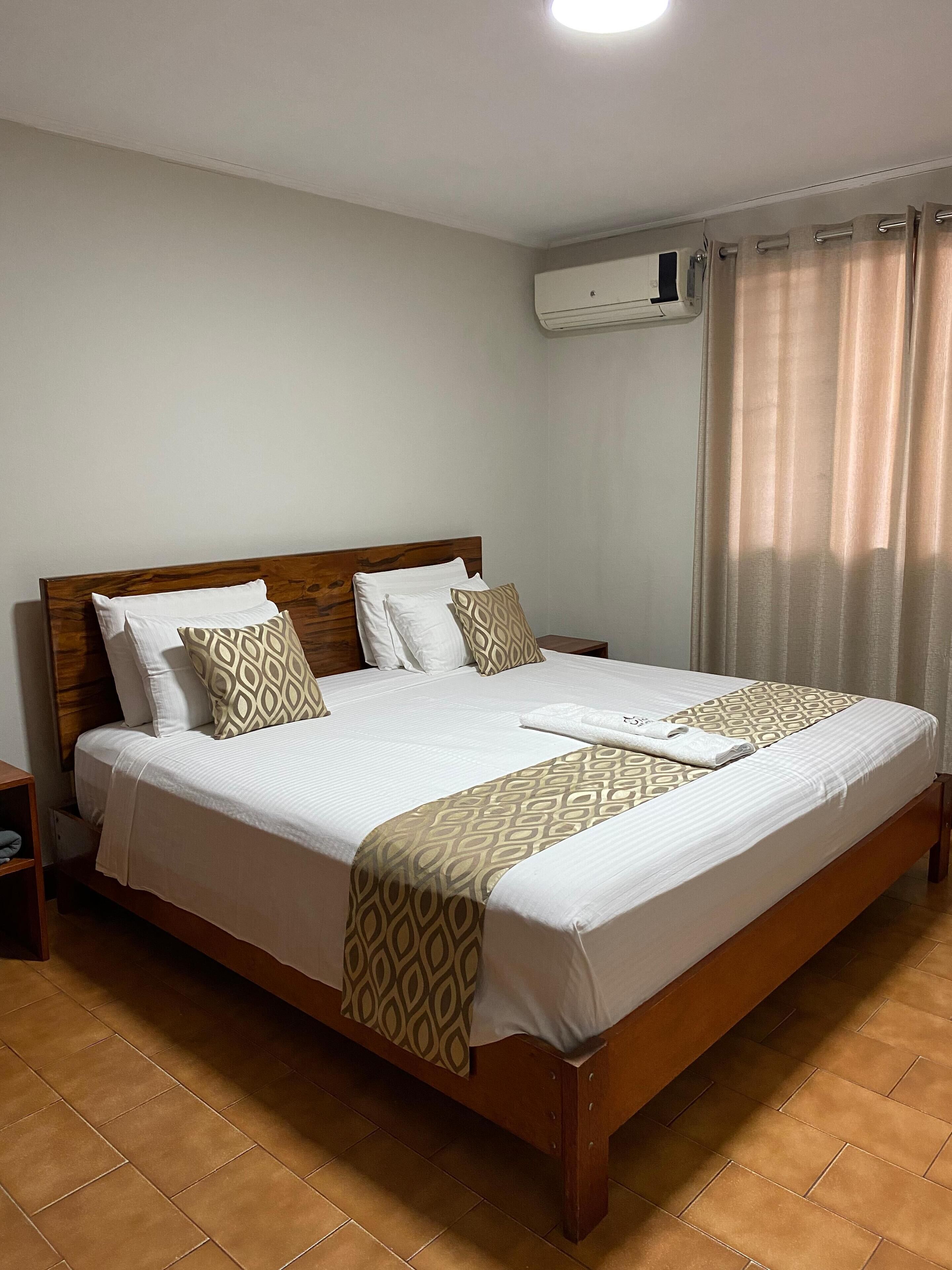 Una cama bien tendida con cabecera de madera, ropa de cama blanca y almohadones estampados.