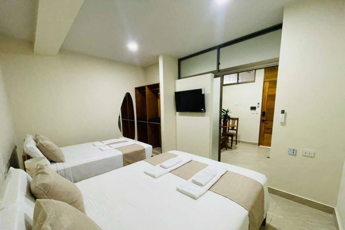 A hotel room with two beds, a TV, and a sliding door leading to a dining area.