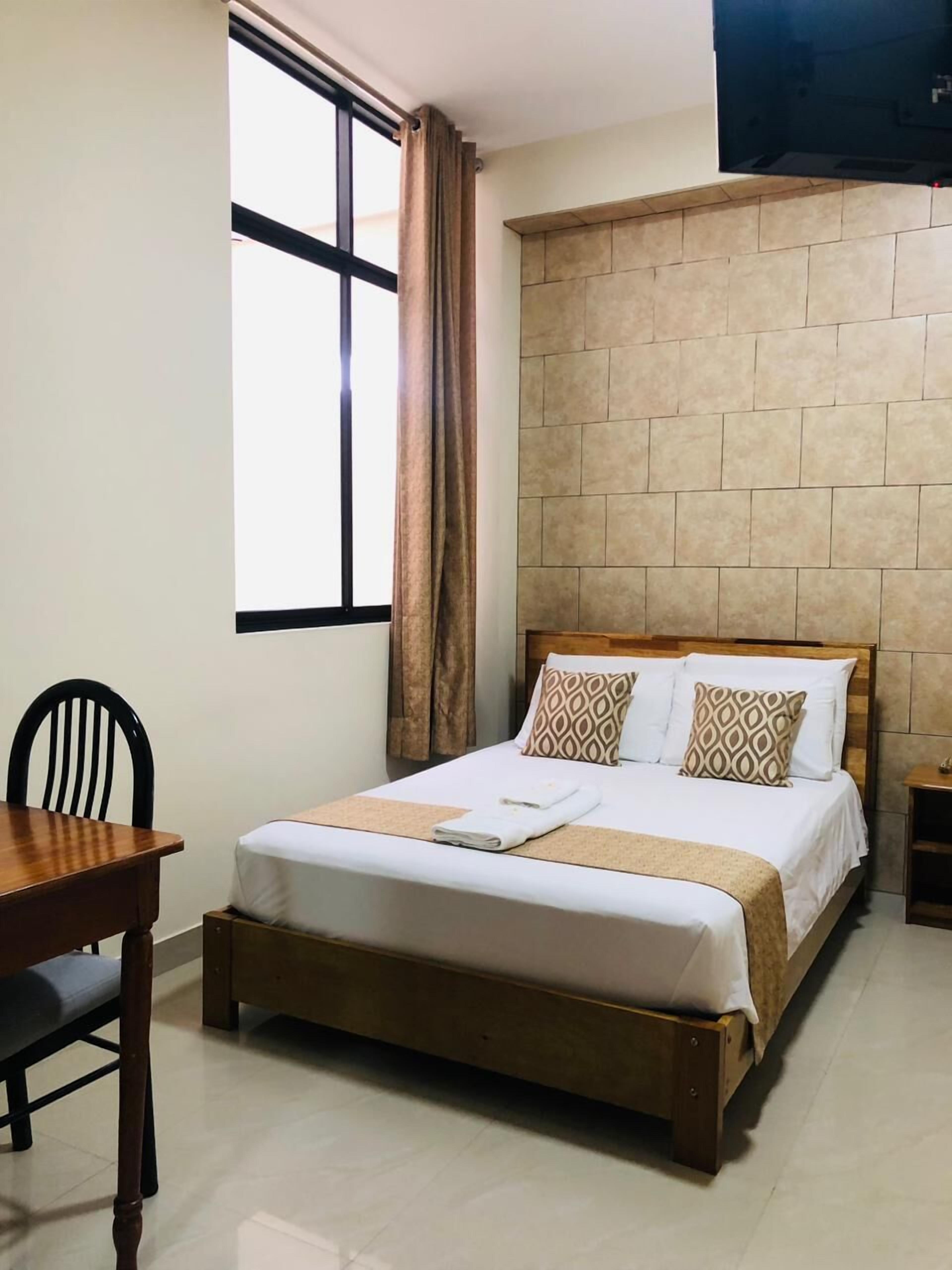 A neatly arranged hotel room with a bed, a wooden nightstand, a chair, and a window with curtains.