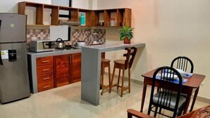 A compact kitchen with wooden cabinets, a refrigerator, a microwave, and a small dining area with two chairs and a table. - Studio 69 (Iquitos)