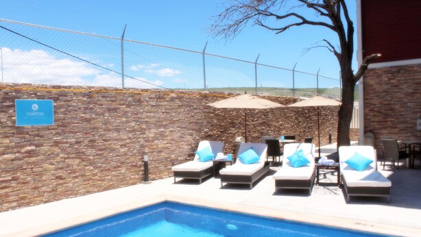 A pool area with lounge chairs and umbrellas, a stone wall, and a sign that reads "noktos". - NOKTOS Extended Chihuahua (Chihuahua)