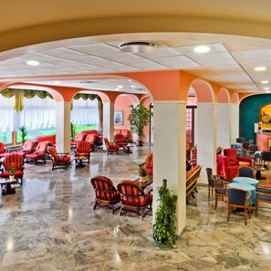 Un lobby amplio con sillones tapizados en rojo, una zona de bar y vistas a un paisaje verde a través de las ventanas.