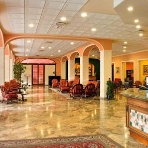 Un hall d’entrée spacieux avec un sol en marbre, plusieurs espaces de détente avec des fauteuils et un comptoir d’accueil.